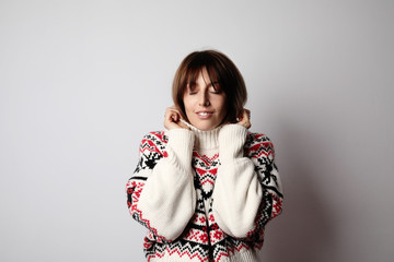 Young woman wearing warm sweater and posing on white wall. Isolated.