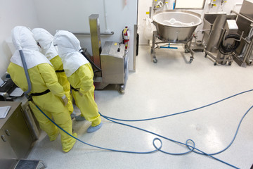 Pharmaceutical workers wearing hazmat suits standing in factory