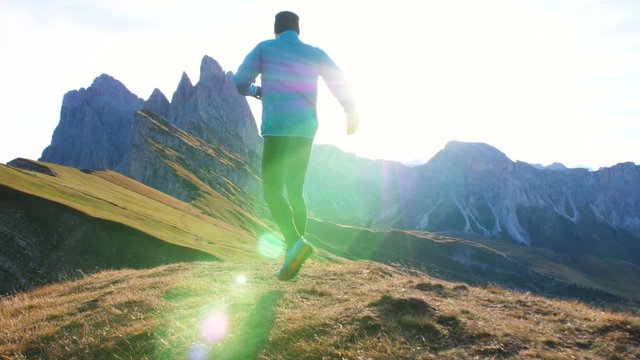 Young man in sport trail clothes running on Seceda mountain peak at sunrise. Puez Odle, Trentino, Dolomites, Italy.
