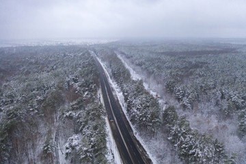 Fototapeta premium The road in a snowy forest. Aerial view. Snow covered tree crowns. North region of Ukraine.