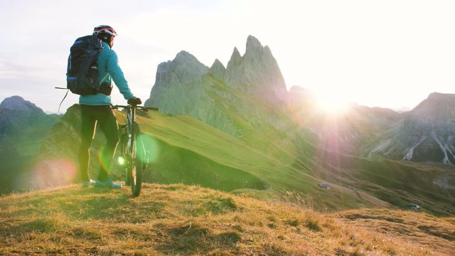 Young man with mountain bike standing on Seceda mountain peak at sunrise. Puez Odle, Trentino, Dolomites, Italy.