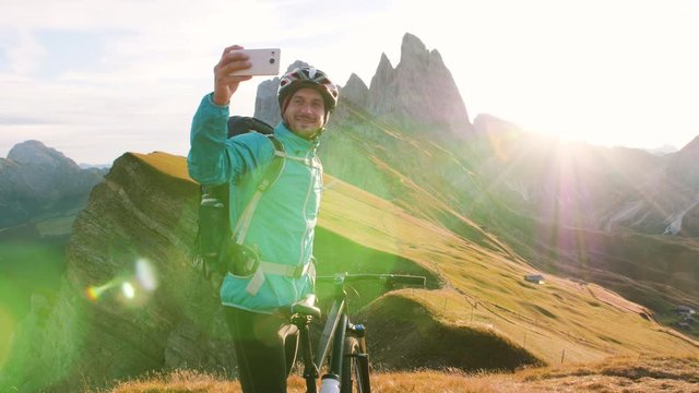 Young man with mountain bike taking selfies on Seceda mountain peak at sunrise. Puez Odle, Trentino, Dolomites, Italy.