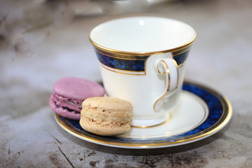 Two vegan gluten free macarons on a saucer beside a tea cup