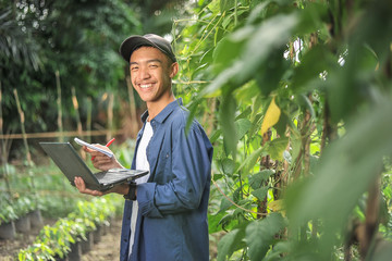 Young Asian farmer man holding laptop at the garden