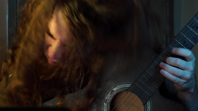Head banging long auburn hair bearded man playing guitar alone close up