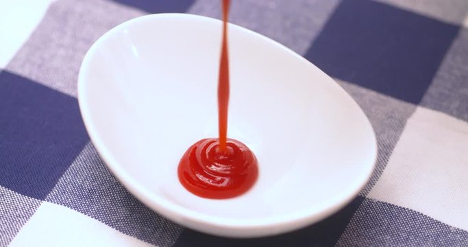 Squirting ketchup into a small, white dish.