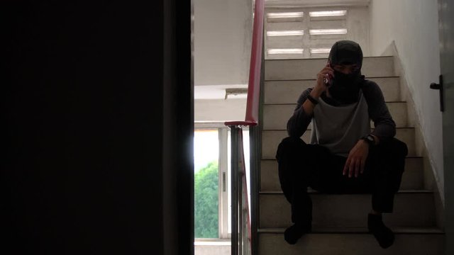 Angry killer in balaclava talking on phone, holding gun and planning crime, corruption,  threatening interlocutor