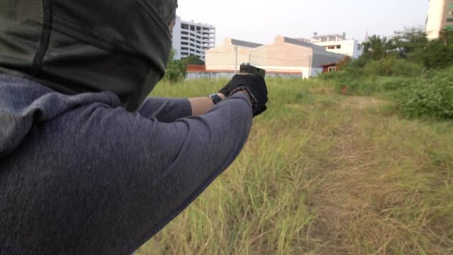 Thief with gun walking in park . Armed burglar in black balaclava holding gun in hands. outdoors. Lifestyle. Crime.