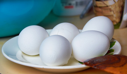Five boiled eggs in a shell on a plate. One egg with cracks in a scarlet shell. Close-up