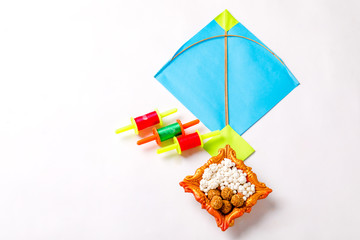colorful paper kite with sesame seed ball or til ke laddo and tilgul in bowl on white background for indian festival makar sankranti 
