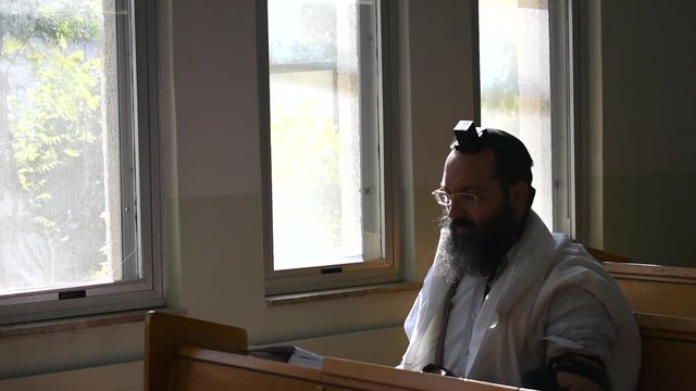 Jewish prayer. Ashkenazi synagogue. Orthodox Jew, with tefillin and tallit, holds up a Sefer Torah.