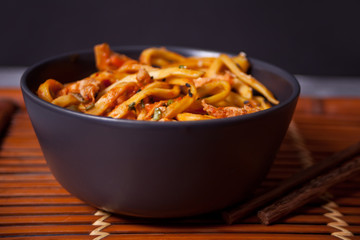 Udon noodles with chicken meat in bowl with chopsticks on dark stone background.