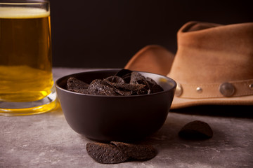 Mexican corn chips nachos, glass of beer and cowboy hat. Black chips nachos for brutal men.