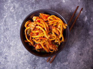 Udon noodles with chicken meat in bowl on dark stone background. Copy space. Top view.