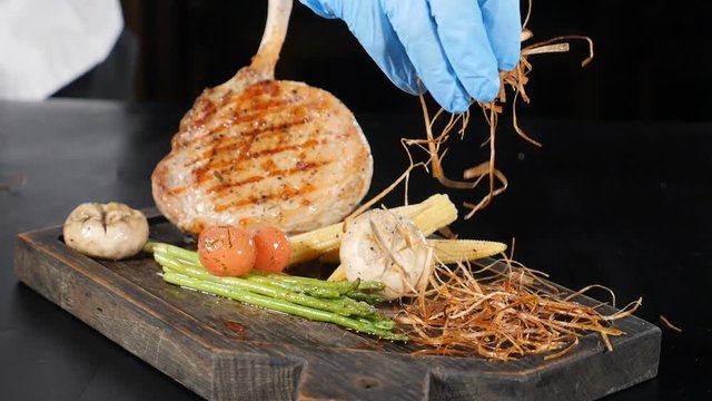 Chef adding herbs and fried onios to restaurant dish with grilled steak and vegetables. Food video in slow motion for commercial usage. Full hd