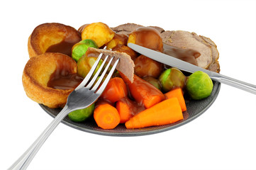Traditional roast beef dinner with roasted potatoes and Yorkshire pudding and vegetables, isolated on a white background