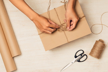 Making gift with soul. Close-up image of man tying a bow on gift box while sitting
