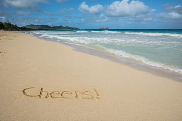 Fototapeta premium Cheers written in the sand on Waimanalo Beach in Hawaii with the ocean in the background