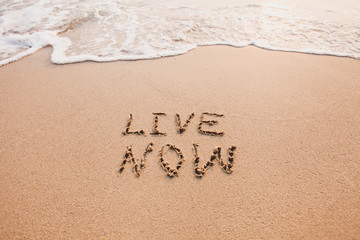 Fototapeta na wymiar live now, mindfulness concept, text written on the sand
