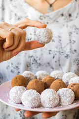 Woman holds sweet vegan coconut balls. Protein energy bars with dates and cocoa. Vegan, vegetarian healthy dessert.
