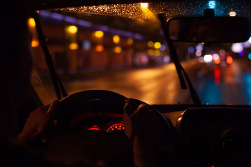 driving car in night city, hands of driver on steering wheel and street lights