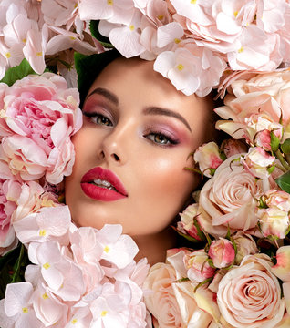 Beautiful white girl with flowers. Stunning brunette girl with big bouquet flowers of roses. Closeup face of young beautiful woman with a healthy clean skin. Pretty woman with bright makeup