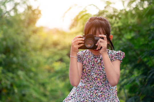 Asian little child girl holding film camera and taking photo with of green natural background