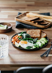 Fototapeta na wymiar Healthy breakfast or lunch at home or cafe with fried egg, avocado, toasts, beans and fresh spinach on a wooden table.