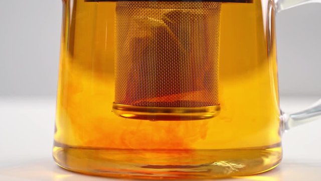 Brewing and steeping black tea leaf in teabag into glass transparent tea kettle pot with boiled hot water, time-lapse shot, close up view, 4K.