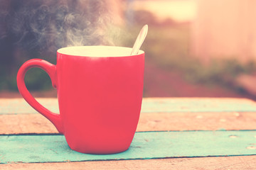 Red mug with hot coffee on a wooden table, natural background