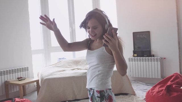 Happy young pretty woman dancing at home having fun listening to music wearing headphones enjoying weekend celebration with funky dance moves
