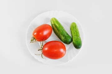 Red ripe juicy tomatoes and green cucumber on a white plate. Light gray background