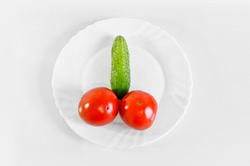 Red ripe juicy tomatoes and green cucumber on a white plate. The phallic image of natural components. Light gray background