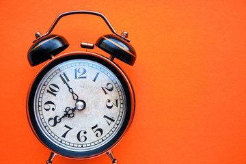 Old, vintage retro alarm clock on a bright orange background.