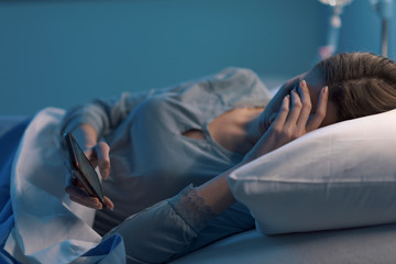 Sad sleepless patient chatting with her phone
