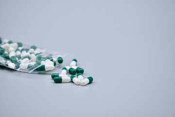 A lot of white and green capsules in the clear plastic bag on the gray background