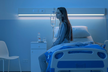 Sad sleepless patient sitting on the hospital bed at night