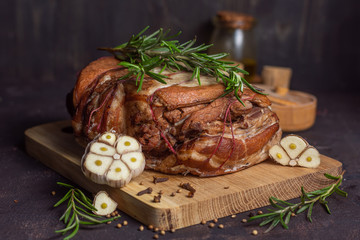 Baked pork brisket with twine on a wooden board with rosemary and spices and garlic on a dark background