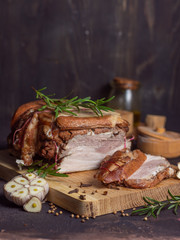 Baked pork brisket with twine on a wooden board.&nbsp;with chopped slices of brisket with rosemary and spices and garlic on a dark background vertical arrangement