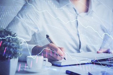 Double exposure of man's hands writing notes of stock market with forex chart.