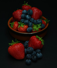 Fresh red strawberries with blueberries in a bowl on black background