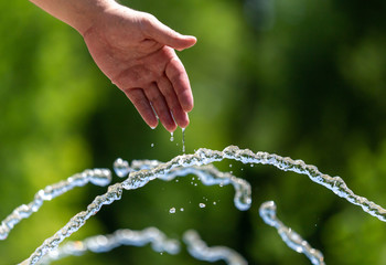 Naklejka na ściany i meble Hand of a man in the spray of water of the fountain