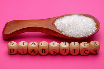 Health concept. Sugar in a wooden spoon with a DIABETES wording on pink background