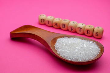 Health concept. Sugar in a wooden spoon with a DIABETES wording on pink background