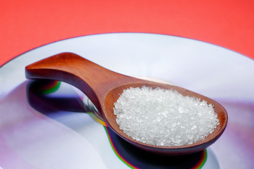 Health concept. Sugar in a wooden spoon on red background