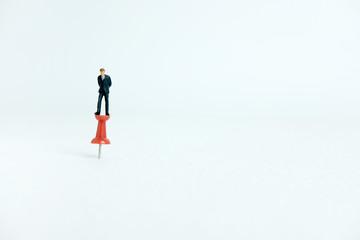 Miniature business concept - a businessman standing on a thumbtack / push pin with white background