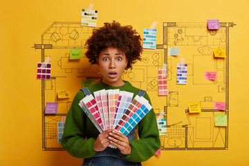 Shocked female decorator holds color palette samples, makes architectural designing plans for...