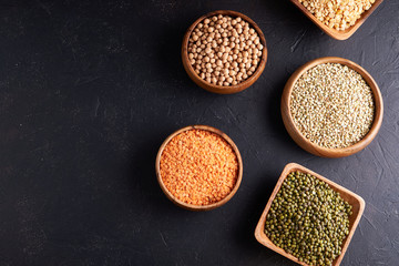 Assortment of cereals, legumes, cereals, grains, lentils, chickpeas, peas, beans, oatmeal in wooden bowls on a dark background