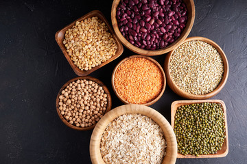 Assortment of cereals, legumes, cereals, grains, lentils, chickpeas, peas, beans, oatmeal in wooden bowls on a dark background