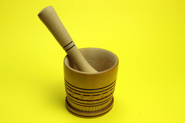 Homemade wooden mortar and pestle on a yellow background